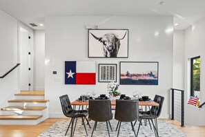 A dining area with a table set for four, a staircase, and a Texas flag on the wall.