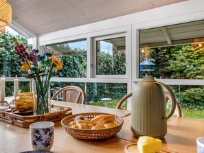 Una mesa de madera con un jarrón de flores, una cesta de pan, una tetera y una taza.