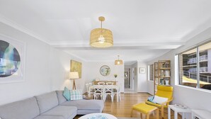 A modern living room with a sofa, a yellow armchair, a dining area, and a large window with a view of a building. - Sunshine and Sea Breeze (SUNSHINE AND SEA BREEZE)