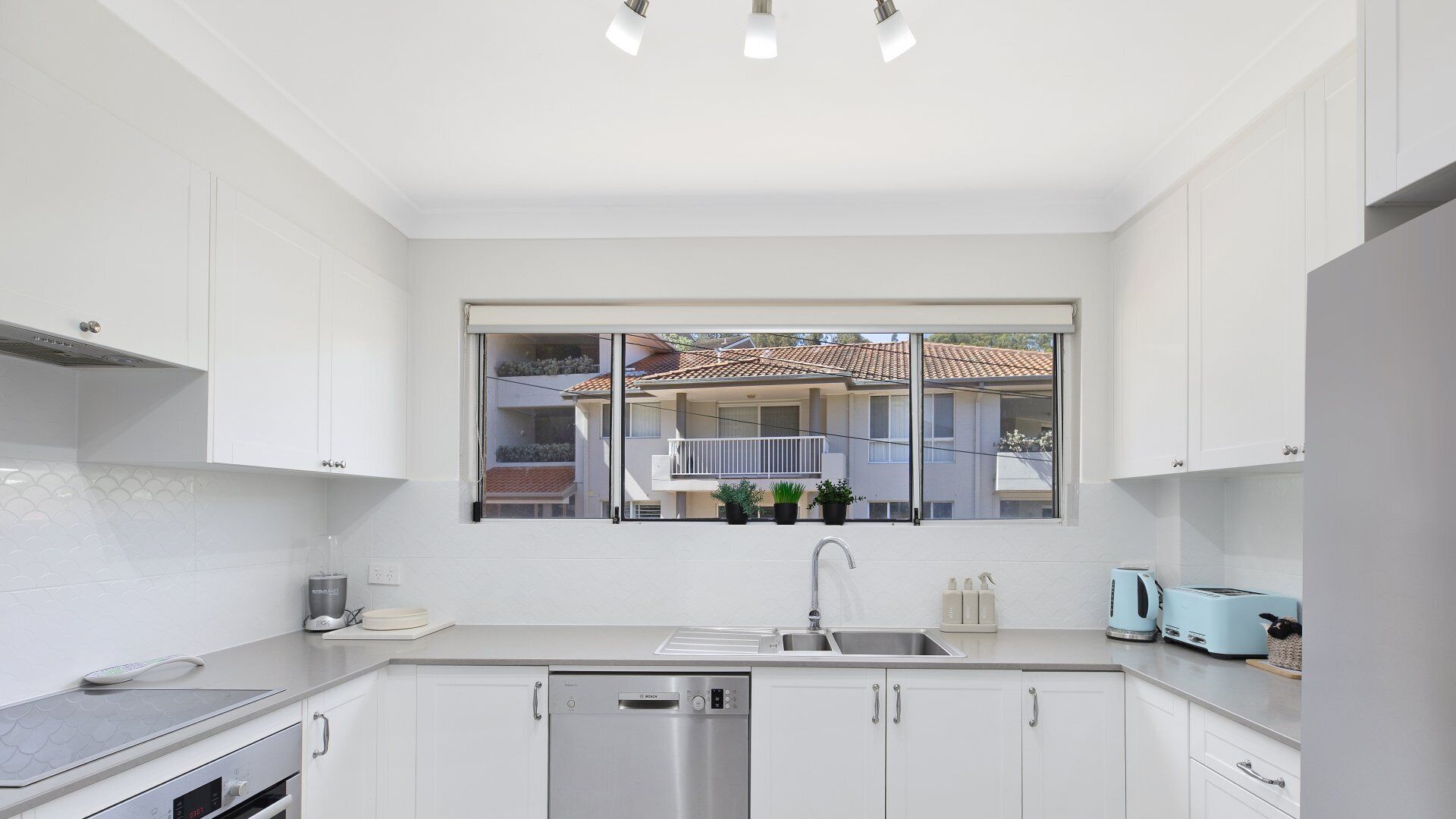 A modern kitchen with white cabinets, a Bosch dishwasher, a sink, and a window overlooking a residential area.