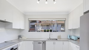 A modern kitchen with white cabinets, a Bosch dishwasher, a sink, and a window overlooking a residential area. - Sunshine and Sea Breeze (SUNSHINE AND SEA BREEZE)