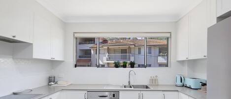 A modern kitchen with white cabinets, a Bosch dishwasher, a sink, and a window overlooking a residential area.