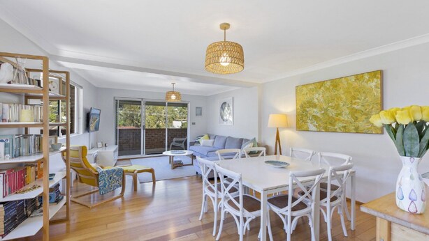 A spacious living area with a dining table, white chairs, a bookshelf, and a large window. - Sunshine and Sea Breeze (SUNSHINE AND SEA BREEZE)