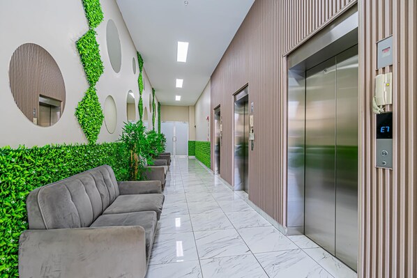 Um lobby moderno com piso de mármore, detalhes verdes na parede, um sofá e um elevador.