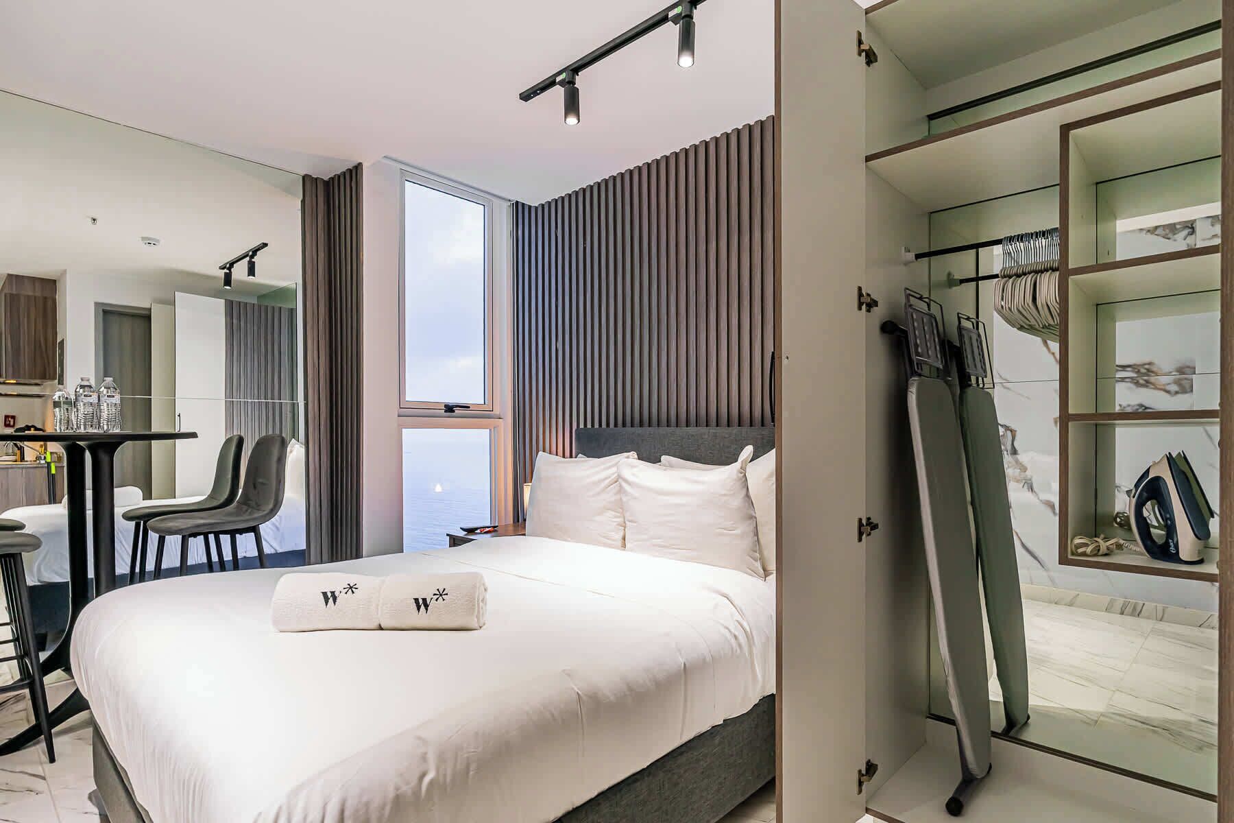 A modern hotel room with a large bed, a desk, and a view of the sea.
