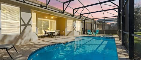An indoor swimming pool with a glass ceiling, a patio area with chairs, and a table.