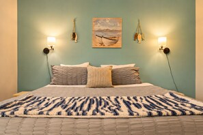 Un letto con una coperta a motivi, due lampade fissate al muro e un quadro raffigurante una barca.