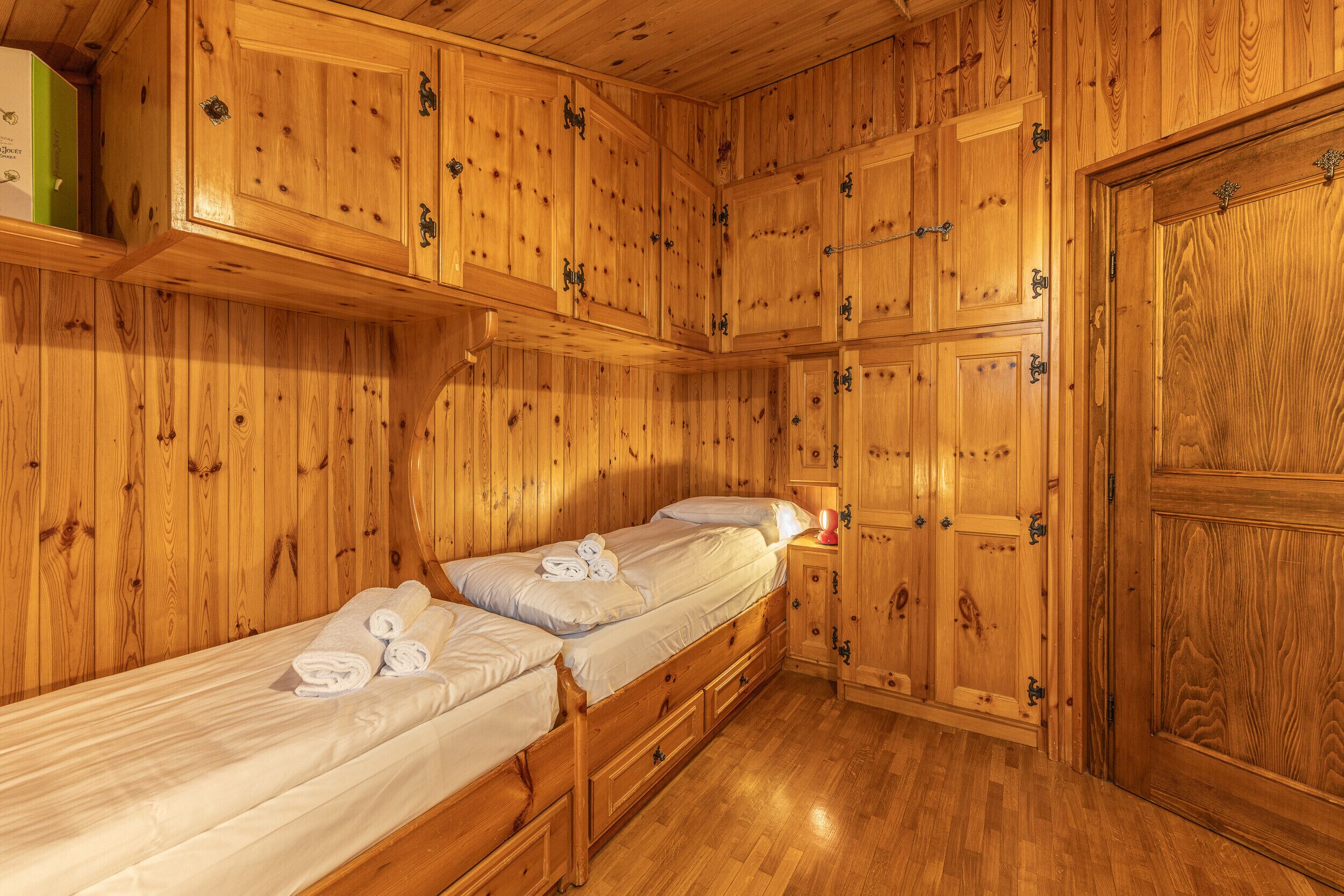 Une chambre dans un chalet en bois, avec deux lits simples, des armoires en bois et une grande porte en bois.