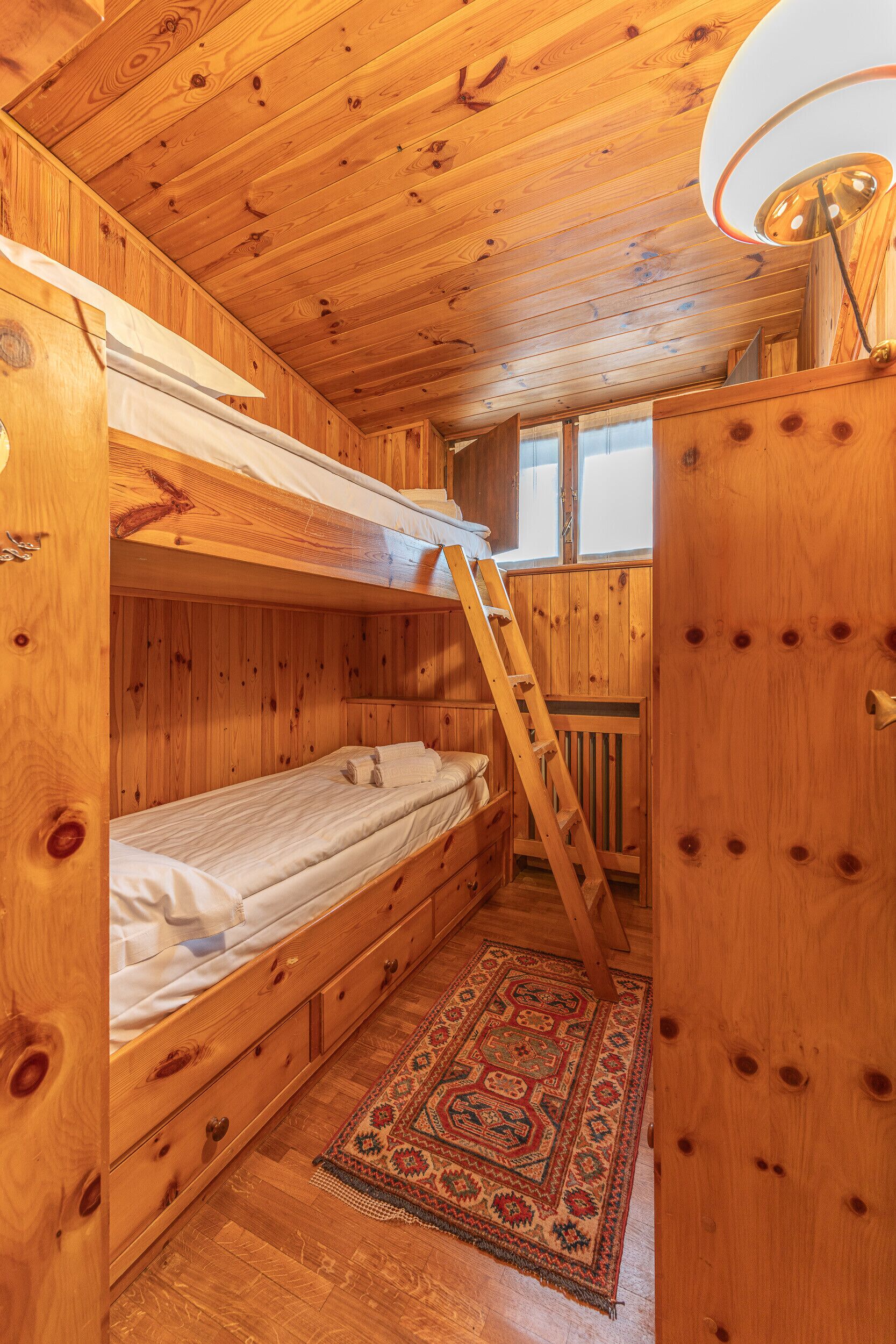 Eine Holzhütte mit Stockbetten, einer Leiter, einem Holzschrank und einem gemusterten Teppich.