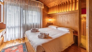 Une chambre à coucher aux murs lambrissés, avec un lit, une table de chevet, une lampe et une fenêtre ornée de rideaux légers.