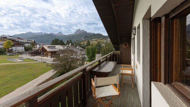 Un balcon avec une balustrade en bois, une table et deux chaises. Un tapis coloré recouvre le sol.