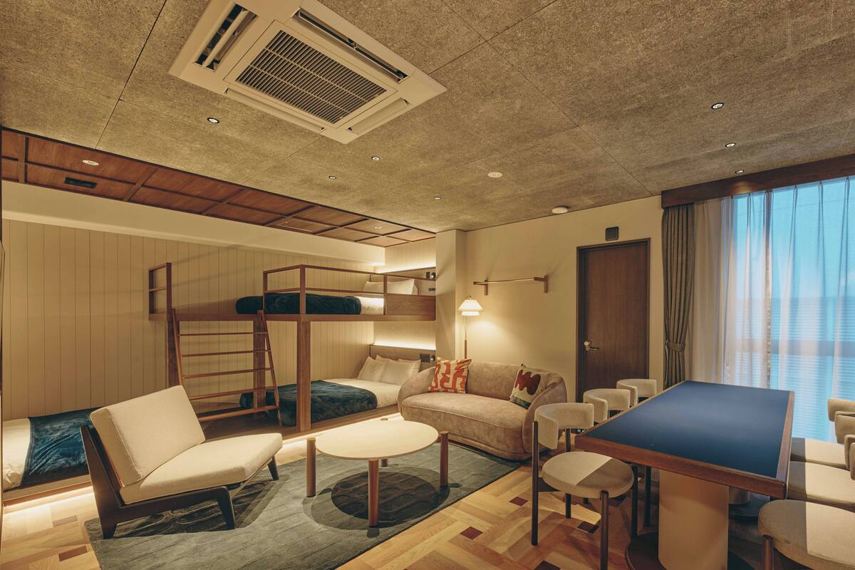 A compact hotel room with bunk beds, a sofa, a dining table, and a small TV.