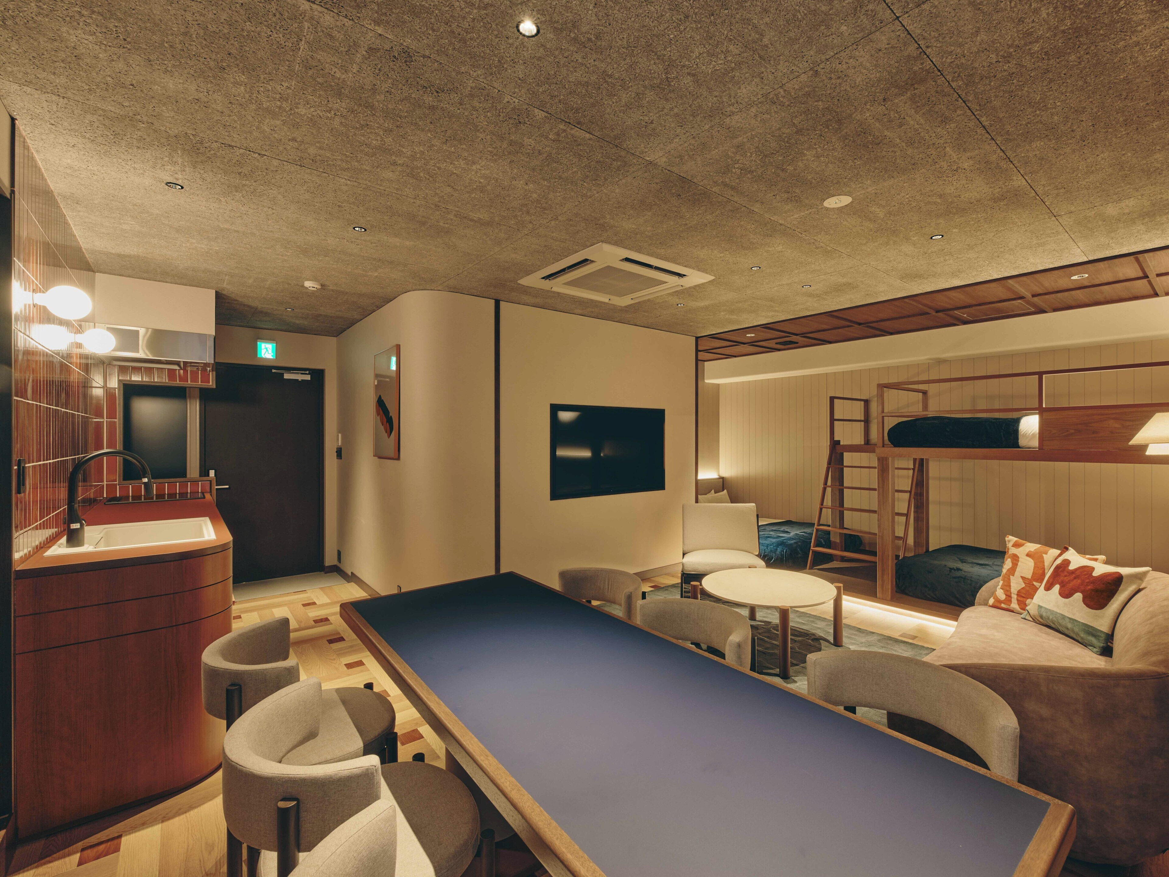 A modern hotel room with a pool table, seating area, bunk beds, and a kitchenette.