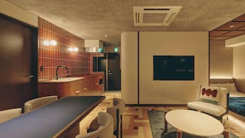 A modern hotel room with a wooden dining table, a sofa, and a TV mounted on the wall.