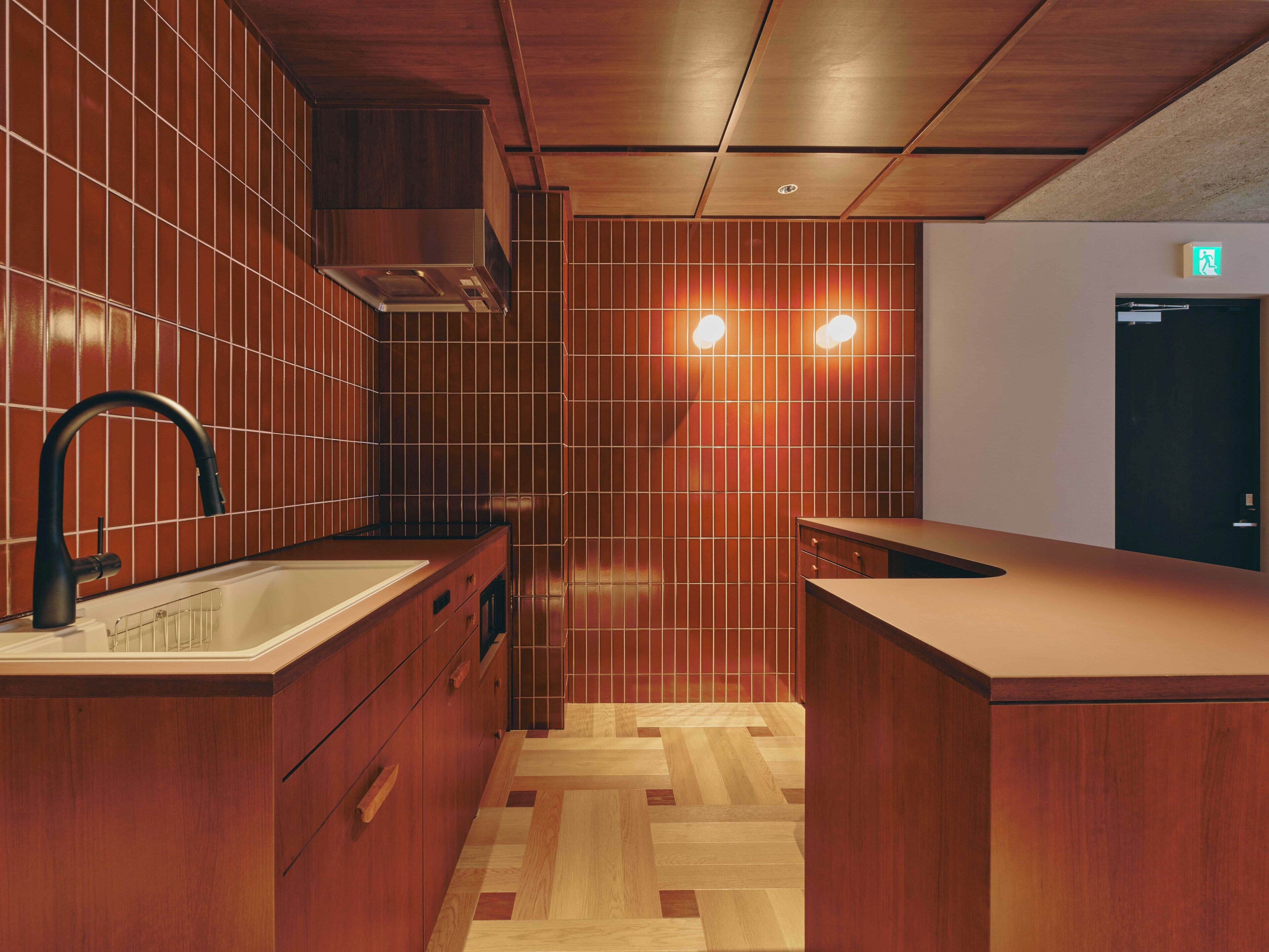 A modern kitchen with wooden cabinetry, a stainless steel sink, and a herringbone-patterned floor.