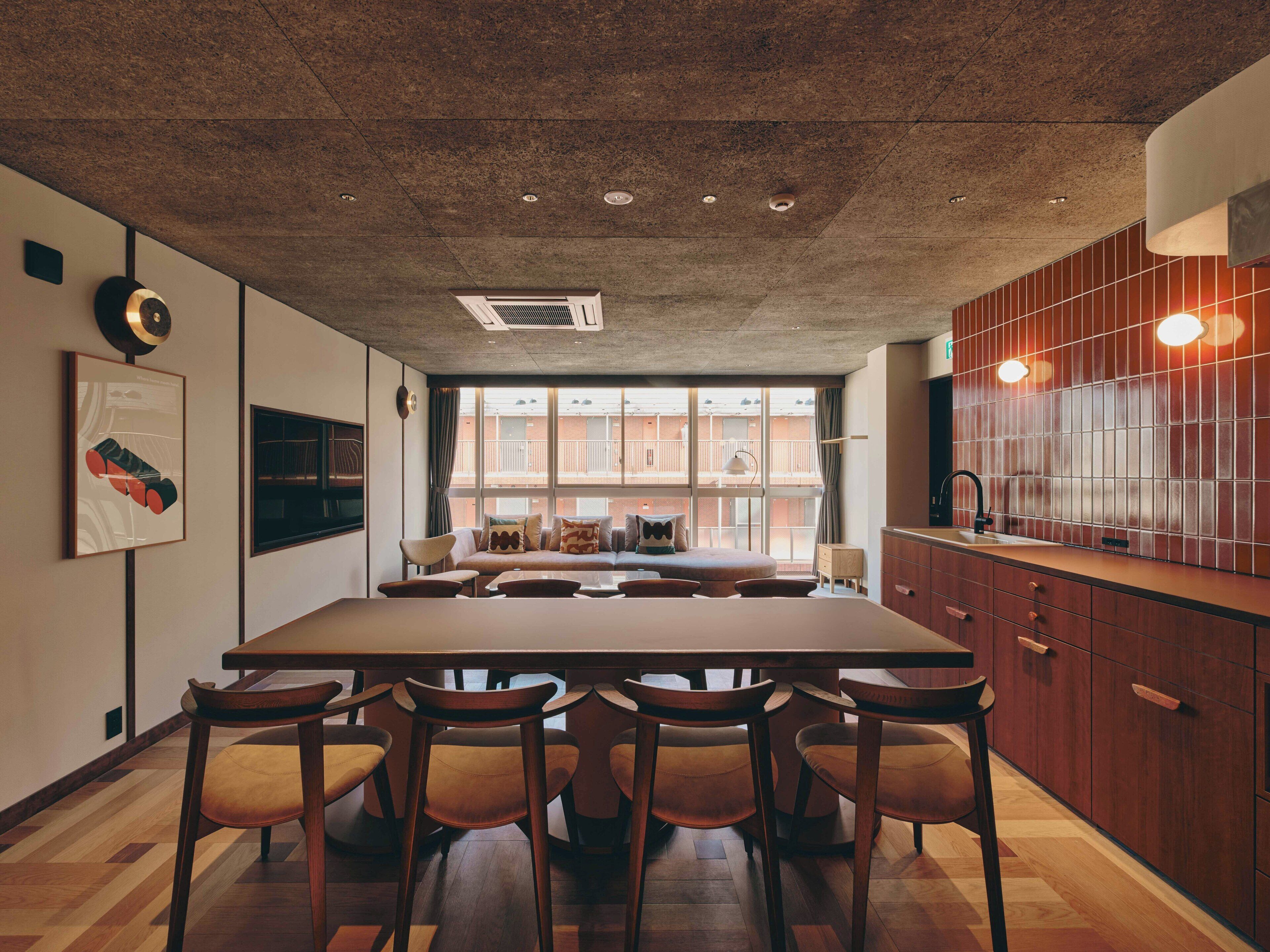 A modern kitchen with a large island, wooden chairs, and a view of a building through the window.