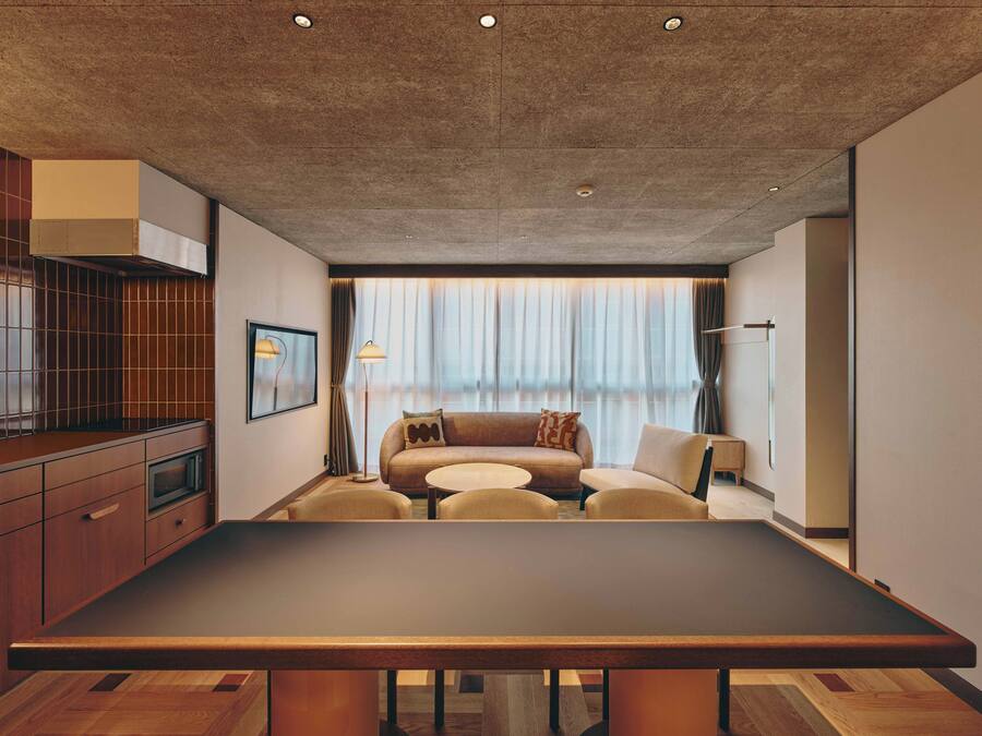 A modern hotel room with a dining table, sofa, and a large window with curtains.