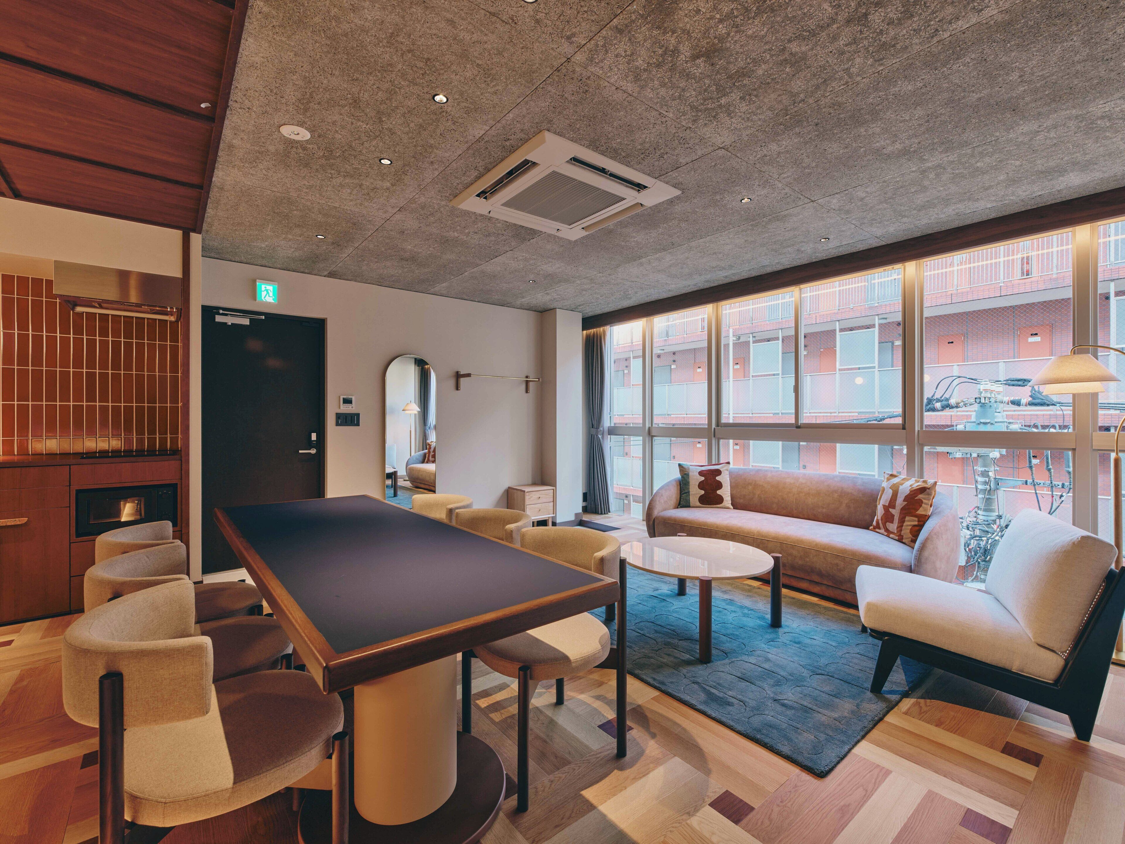 Habitació d'hotel moderna amb un gran menjador, seients còmodes, un sofà i grans finestres que ofereixen vista a la ciutat.