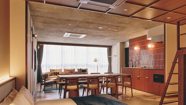 A modern hotel room with a large bed, a dining area with a wooden table and chairs, a kitchen area with wooden cabinets, and a large window providing natural light. - illi Nuto Shinjuku (Tokyo)