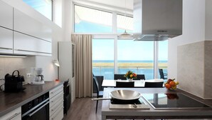 A modern kitchen with a large window, a dining area with a view, and a built-in stove. - Beachfront Penthouse Apartment in Marina Wendtorf with Stunning Sea View (Wendtorf)