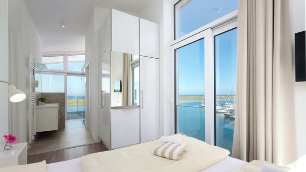 A modern hotel room with a large window offering a view of the sea and boats. - Beachfront Penthouse Apartment in Marina Wendtorf with Stunning Sea View (Wendtorf)