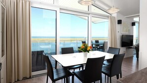 A modern dining area with a large table and chairs, large windows with a view of the sea, and a flat-screen TV on the wall. - Beachfront Penthouse Apartment in Marina Wendtorf with Stunning Sea View (Wendtorf)