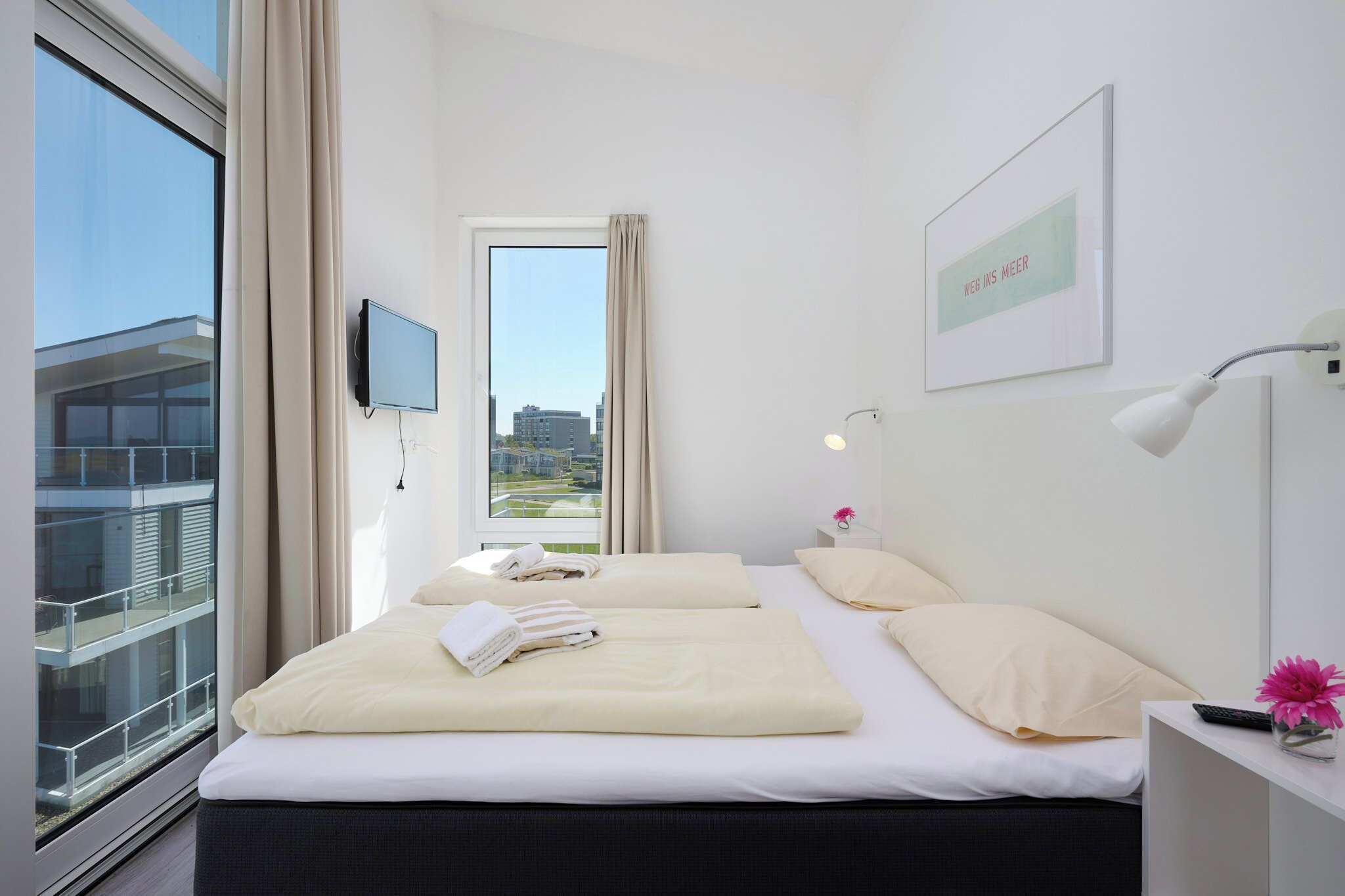 Een hotelkamer met twee bedden, een televisie, een raam met uitzicht op gebouwen en een ingelijst schilderij aan de muur.