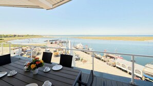A balcony with a table set for dining, overlooking a marina with boats and a calm body of water. - Beachfront Penthouse Apartment in Marina Wendtorf with Stunning Sea View (Wendtorf)