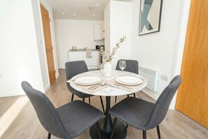 A dining area with a round table, four grey chairs, a vase with a plant, and a framed picture on the wall. - Bright 2 Bed Apartment in Nottingham Centre (Nottingham)