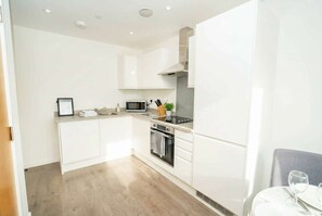 A modern kitchen with white cabinetry, a microwave, an oven, and a dining area with a table and chairs. - Bright 2 Bed Apartment in Nottingham Centre (Nottingham)