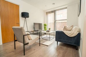 A modern living room with a sofa, armchair, TV, and a floor lamp. - Bright 2 Bed Apartment in Nottingham Centre (Nottingham)