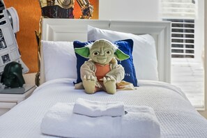 Ein Bett mit Kuscheltier, weißer Bettwäsche und einem Fenster mit Jalousien.