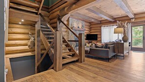 Un escalier en bois mène à une chambre située en mezzanine, qui comprend une cheminée en pierre, un téléviseur à écran plat et un canapé dans un coin salon confortable.
