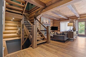 Eine Holztreppe führt zu einem Schlafzimmer auf dem Dachboden, mit Kamin aus Stein, Flachbildfernseher und einer Couch in einem gemütlichen Wohnbereich.