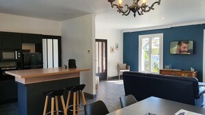 Une cuisine moderne dotée d’un îlot central, un coin repas avec une table et des chaises, un salon avec un canapé et un téléviseur fixé au mur.