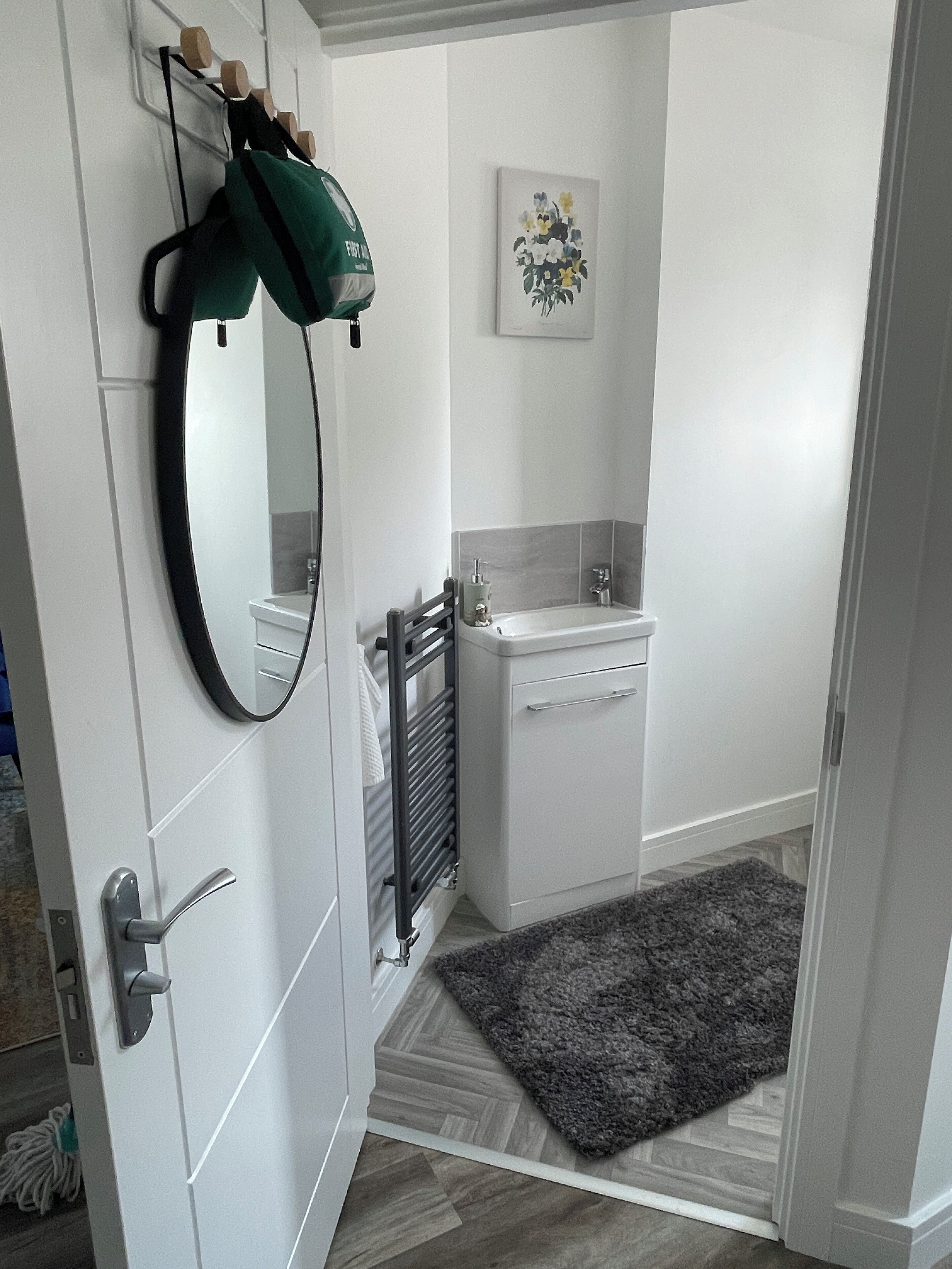 Un baño con un lavamanos blanco, un espejo y un perchero para toallas.