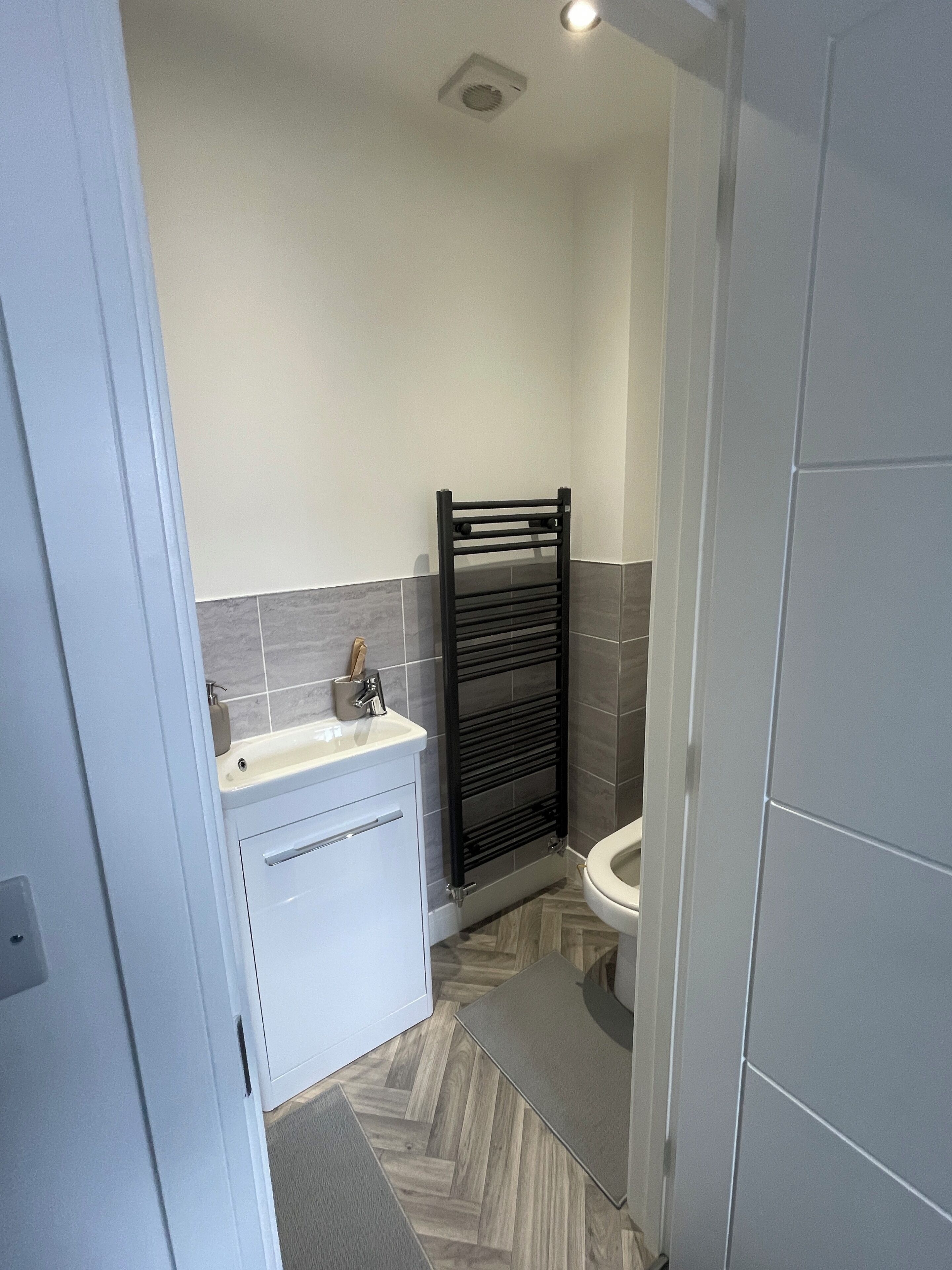 A modern bathroom with a white sink, black towel rack, and a toilet.