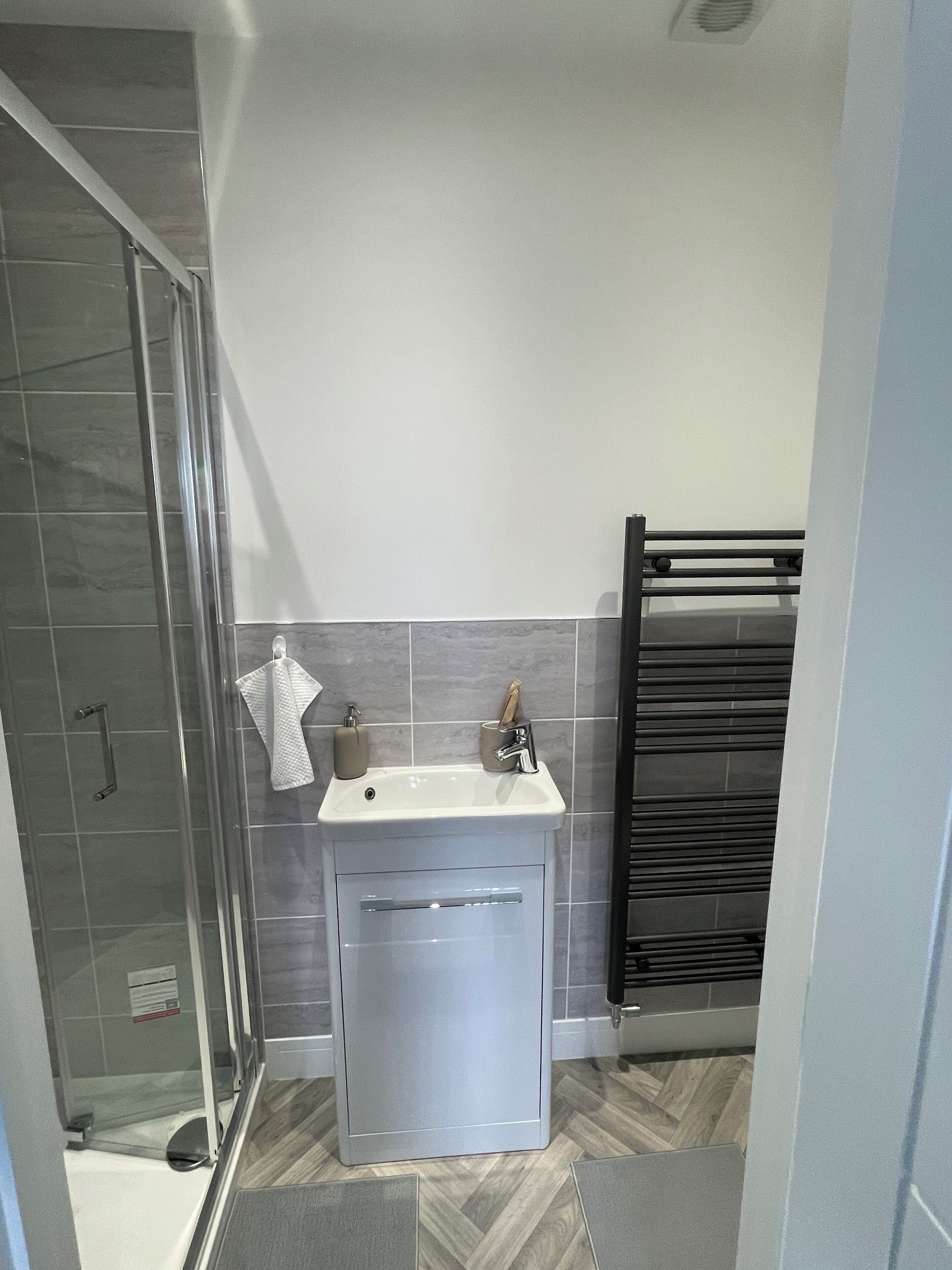 A bathroom with a glass shower enclosure, a white sink with a soap dispenser, and a towel rack.