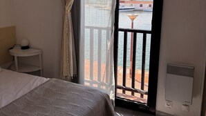 Ein Hotelzimmer mit Bett, einem kleinen Nachttisch, einem Fenster mit Meerblick und einem Balkon mit Geländer.