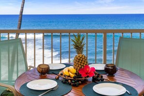 A table set for two with a view of the ocean, a pineapple, bananas, and a hibiscus flower. - Ocean Front Deluxe Top Floor AC Concierge Included - Vrkcv (Kailua-Kona)