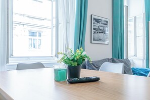 A hotel room with a wooden table, a potted plant, a remote control, and a window with curtains. - Value 2BR Apt Central City Location (Vienna)