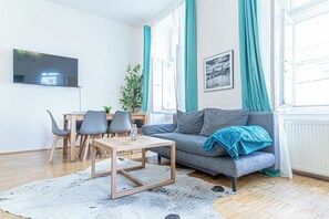 A modern living room with a grey sofa, wooden coffee table, and a dining area with chairs and a table. - Value 2BR Apt Central City Location (Vienna)