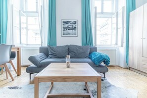 A modern living room with a grey sofa, a wooden coffee table, and a cityscape framed picture on the wall. - Value 2BR Apt Central City Location (Vienna)
