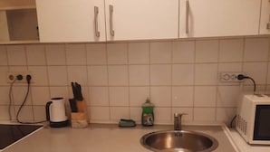 Ett kök med vita skåp, en diskho i rostfritt stål, en mikrovågsugn och en vattenkokare.