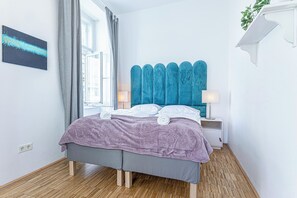 Ein modernes Schlafzimmer mit Bett, Nachttisch, Lampe und einem Fenster mit Vorhängen.