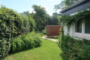 Un jardín con un cobertizo de madera, un sendero y una casa con ventana.