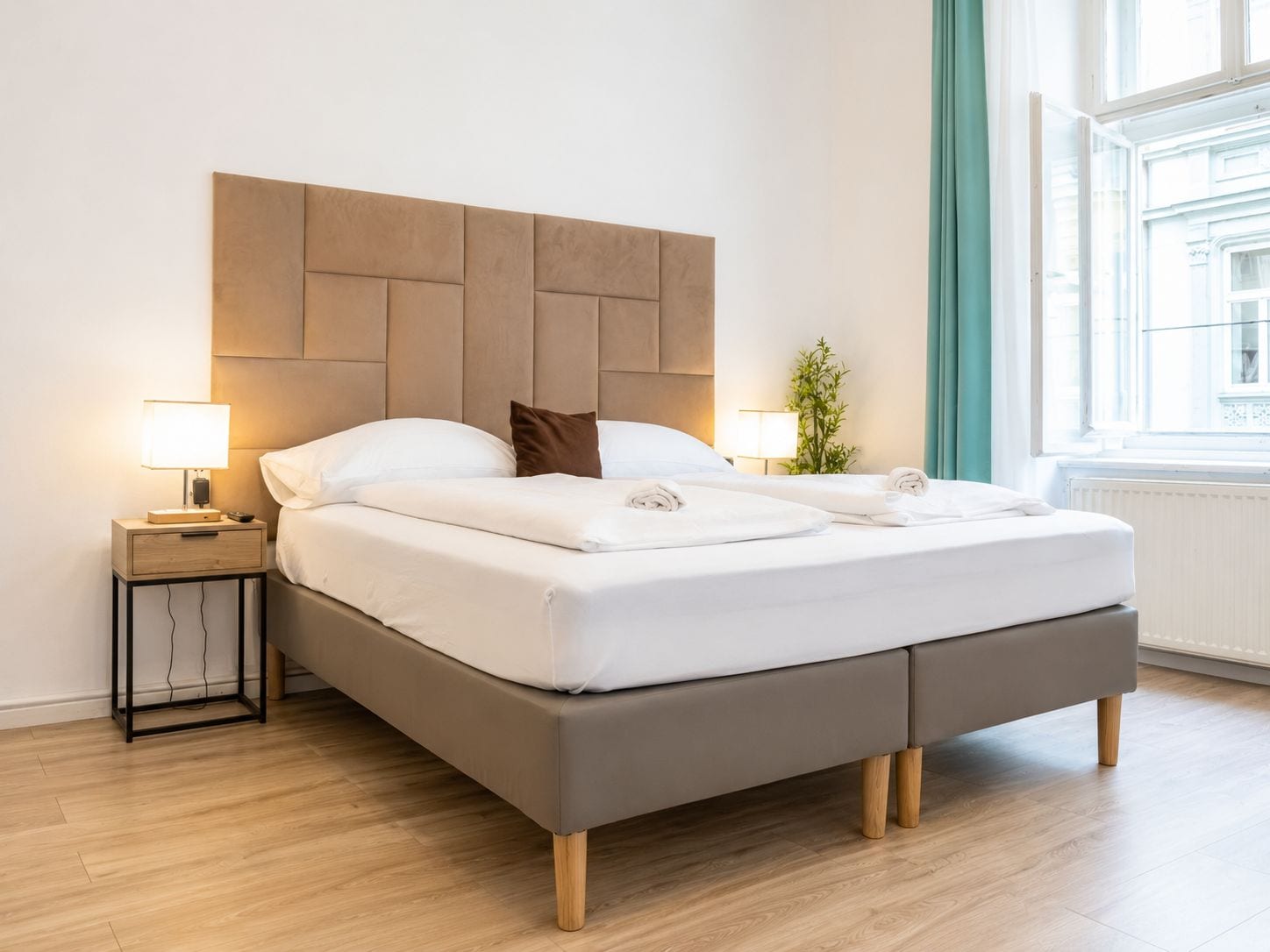 Ein modernes Hotelzimmer mit einem großen Bett, Nachttischlampen, einer Pflanze und Blick auf die Stadt durch das Fenster.