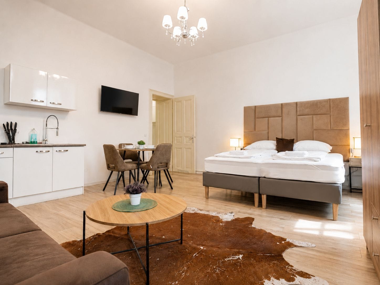 A modern hotel room with a bed, a dining area, a kitchen, and a living space.