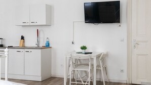 Ett modernt kök med vita skåp, en matplats med ett vitt bord och stolar samt en väggmonterad platt-TV.