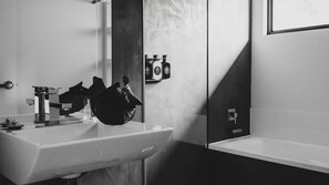 Et moderne badeværelse med en hvid vask, et spejl og et sort håndklæde hængende på væggen.